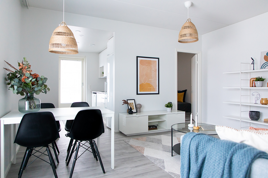 Olohuone, jossa on moderni sisustus. Harmaa sohva, musta kahvipöytä ja valkoinen ruokapöytä luovat minimalistisen ilmeen. Taustalla oleva abstrakti taulu lisää huoneeseen luonnetta.