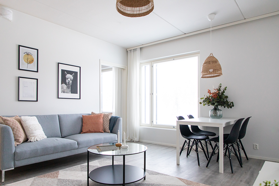 Olohuoneeseen on sijoitettu harmaa sohva, ruokailuryhmä ja asunto on sisustettu harmaalla ja ripauksella oranssia.